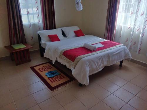 1 dormitorio con 1 cama con sábanas blancas y almohadas rojas en La petals hideaway house-Machakos en Machakos