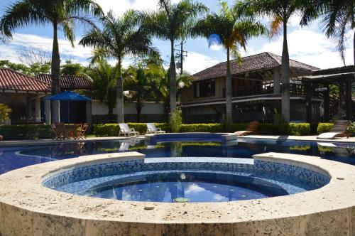 a large swimming pool with a large house and palm trees at Hotel Boutique Villas de San Sebastián in Villavicencio