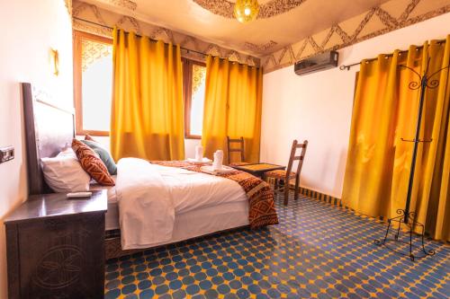 a bedroom with a bed with yellow curtains and a table at Riad Merzouga Dunes in Merzouga