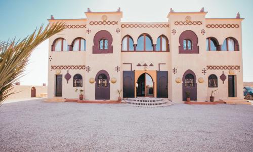 a house with a palm tree in front of it at Riad Merzouga Dunes in Merzouga