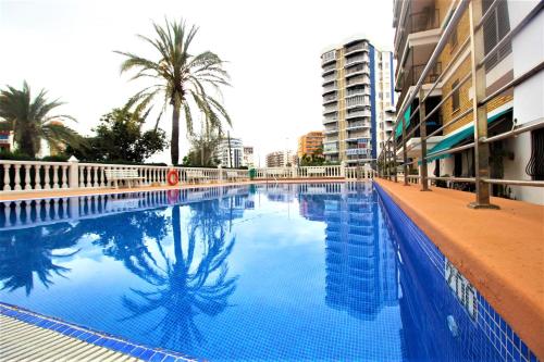 uma grande piscina azul com palmeiras e edifícios em Precioso apartamento con piscina WiFi em La Pobla de Farnals