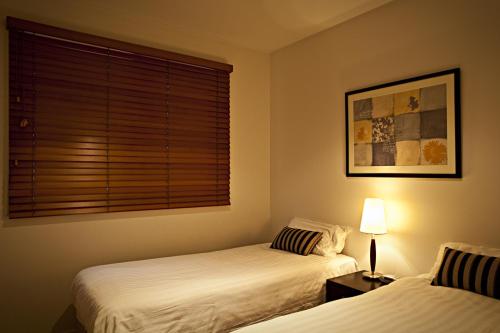 two beds in a room with a window and a lamp at Brighton Bay Apartments in Melbourne