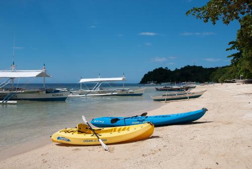 two kayaks on a beach with boats in the water at Easy Diving and Beach Resort in Sipalay