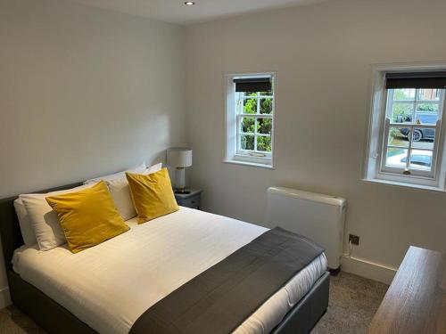 a bedroom with a bed with yellow pillows and two windows at Swan House - 5 x Executive Apartments - Central Bawtry in Bawtry