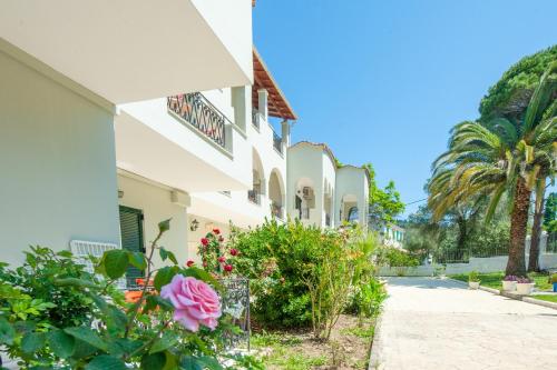 un edificio bianco con fiori e una palma di Vassilis Paradise Garden Aparthotel ad Agios Georgios Pagon