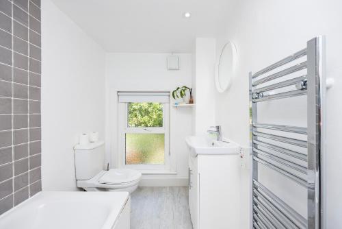 baño blanco con aseo y ventana en WelcomeStay Colliers Wood Two Bed Apartment - Home Away from Home, en Londres