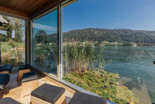 a room with a large window with a view of a lake at Hotel SeeRose in Bodensdorf