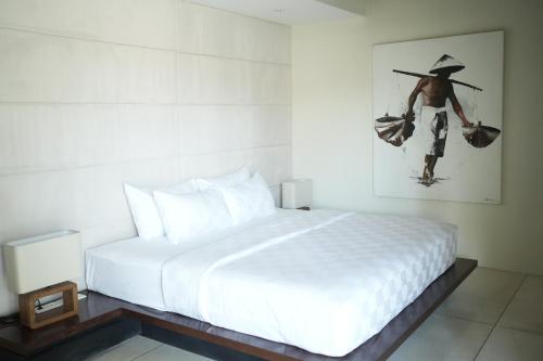 Un dormitorio con una cama blanca y un cuadro de un hombre. en VILLA CELAVI 15, en Kerobokan