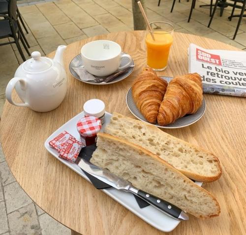 une table avec une assiette de pain, de croissants et de jus d'orange dans l'établissement Hôtel Les Mouettes, à La Couarde-sur-Mer