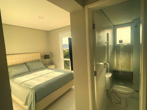 a bedroom with a bed and a bathroom with a toilet at Apartamento 3 suítes Camburi in Camburi