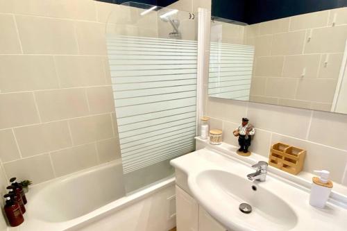 La salle de bains blanche est pourvue d'un lavabo, d'une baignoire et d'un miroir. dans l'établissement Joli T2 en centre-ville Lorient avec balcon cosy, à Lorient