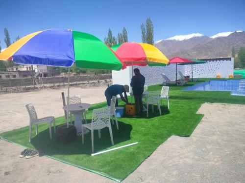 two people standing under umbrellas next to a table and chairs at The Royal Maryul Banquet Hall , Restaurant & Resort - Leh in Stak