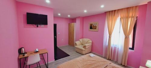 a pink room with a chair and a television on a wall at CityCenterHotel Shkoder in Shkodër