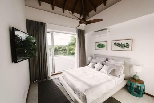 een witte slaapkamer met een bed en een groot raam bij VILLA BELLA LUNA WITH CHEF MAiD GOLF CART AND POOL in Punta Cana