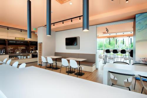 a dining room with white tables and chairs and large windows at B&B Hotel Rostock-Hafen in Rostock