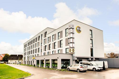 B&B Hotel Ravensburg في رافنسبرغ: مبنى أبيض كبير مع سيارتين متوقفتين في الأمام