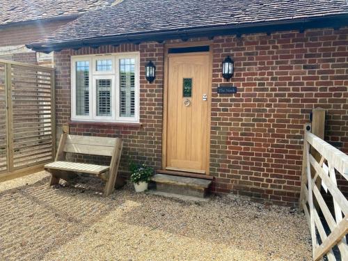 a brick house with a wooden door and a bench at Luxury Self Catering Studio with vaulted ceiling in Ockley