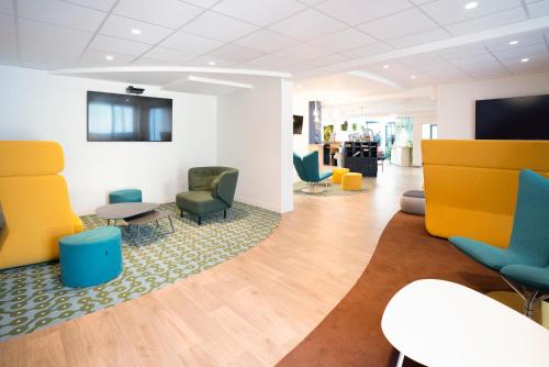 a waiting room with colorful chairs and tables at ibis Styles Fougeres in Beaucé