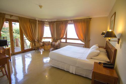 a hotel room with a bed and a desk and windows at Hotel y Cabañas Punta Larga - Caja Los Andes in Frutillar