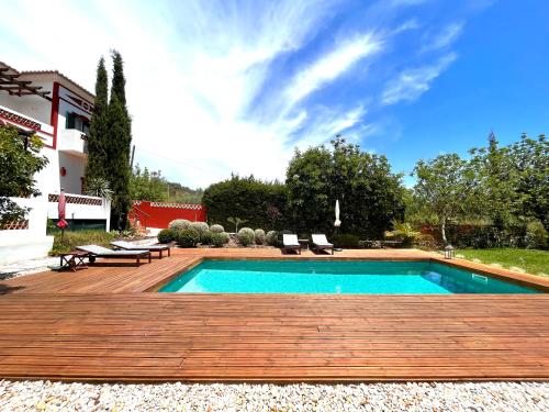 a swimming pool with a wooden deck next to a house at Quinta das Carpas in Tavira