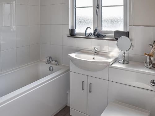 a white bathroom with a sink and a tub and a mirror at Lilys Cottage in Wroxham
