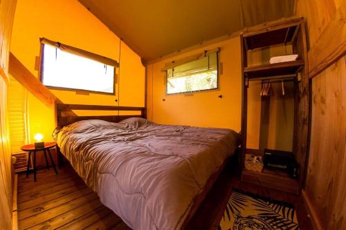 Bett in einem Zimmer mit gelben Wänden und 2 Fenstern in der Unterkunft Camping et Lodges de Coucouzac in Lagorce