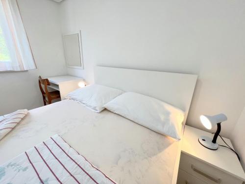 a bedroom with a white bed with a lamp and a desk at MiraMar Gardenn Apartmment in Rab