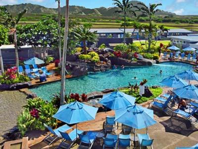 - une piscine avec des chaises et des parasols bleus dans un complexe dans l'établissement Kiahuna Plantation Resort Kauai by OUTRIGGER, à Koloa
