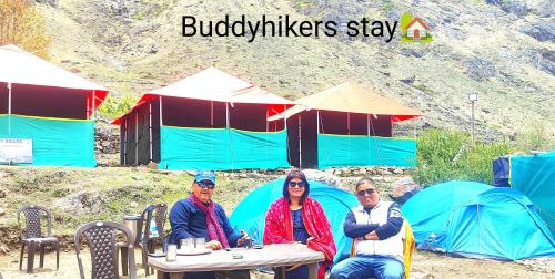 3 Personen sitzen an einem Tisch vor Zelten in der Unterkunft Buddy Hikers Stay Badrinath in Badrīnāth