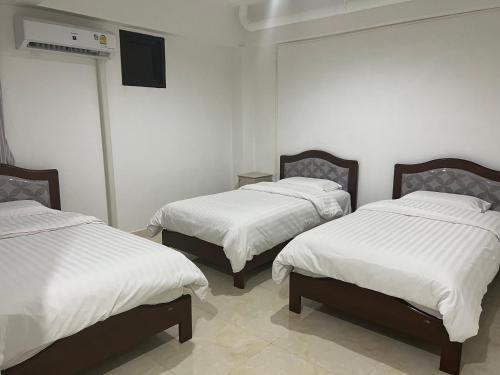 a room with three beds with white sheets and a television at Mall Suites Hotel in Bangkok