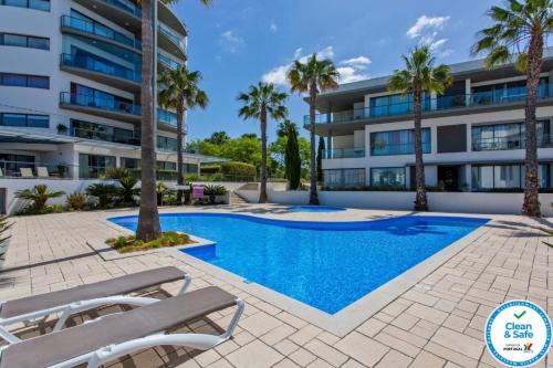 a swimming pool in front of a building with palm trees at Cavalo Preto Beach Residence with Garden & Pool in Quarteira