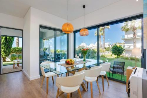 a dining room with a glass table and white chairs at Cavalo Preto Beach Residence with Garden & Pool in Quarteira