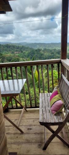 a bench sitting on a wooden porch with a view of the jungle at Bon Mange Organic Farm in Vieux Fort