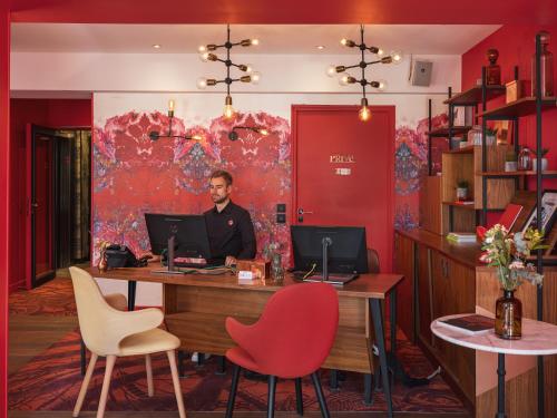 a man sitting at a desk with a computer at Hôtel Exquis in Paris