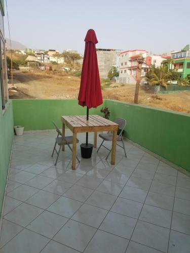 a table with a red umbrella on a balcony at chez albino guest house in São Filipe