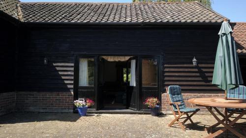 a patio with a table and an umbrella and a table and chairs at Paddock Barn ~ Short & Long term stay, pets welcome ~ Woodbridge, Framlingham ar in Cretingham