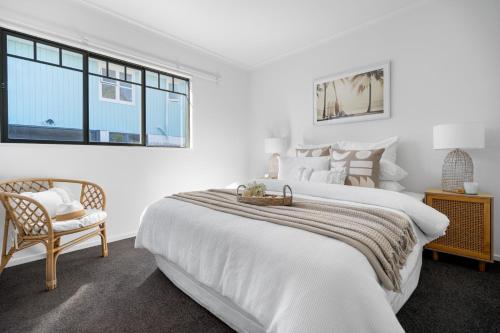 a white bedroom with a large bed and a chair at Seaside Chalet Papamoa in Papamoa