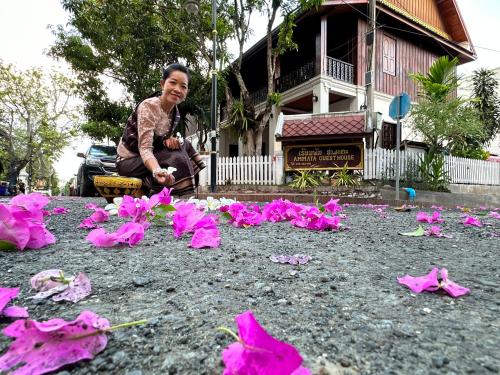 a woman sitting in front of a house with pink flowers at Ammata Boutique Villa in Luang Prabang