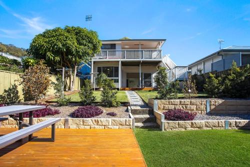 a house with a wooden walkway in front of a yard at Renovated Coastal getaway with water views in Umina