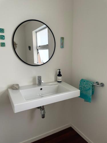 La salle de bains est pourvue d'un lavabo blanc et d'un miroir. dans l'établissement Medlands Beach House, sur l’île de la Grande Barrière