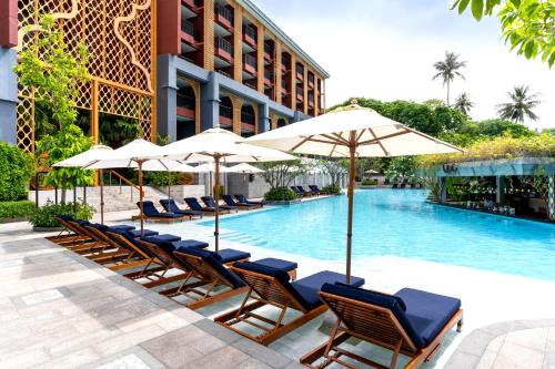 a pool with chairs and umbrellas next to a building at Avista Grande Phuket Karon - MGallery in Karon Beach