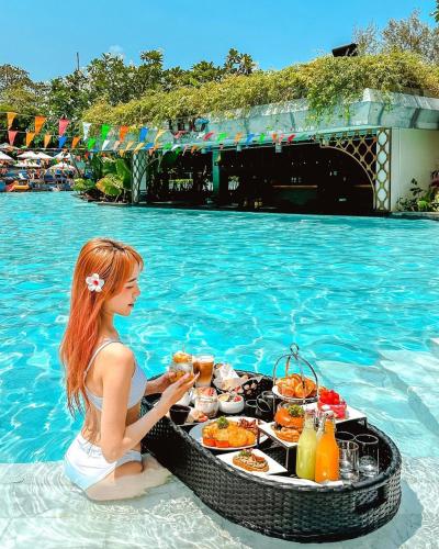 a girl sitting in the water with a tray of food in a swimming pool at Avista Grande Phuket Karon - MGallery in Karon Beach
