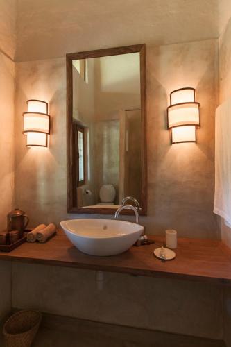 a bathroom with a sink with a mirror and lights at Tiger Tops Karnali Lodge in Bardia