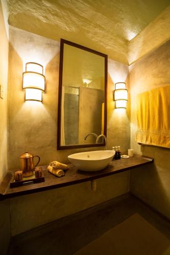 a bathroom with a sink and a mirror and lights at Tiger Tops Karnali Lodge in Bardia