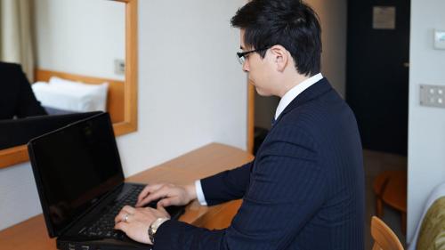 a man in a suit typing on a laptop computer at Hotel Dorf Shizuoka in Shizuoka