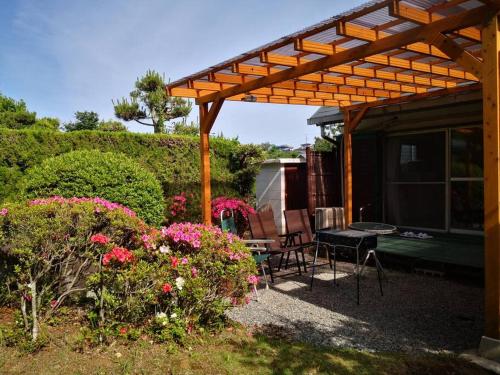 a patio with a wooden pergola and chairs and flowers at ボルダリング＆SPA-安吏樹リゾート修善寺ANNEX- in Izu