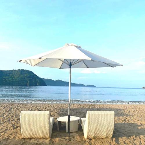 two chairs and an umbrella on the beach at Pico De Loro Room Rental in Nasugbu