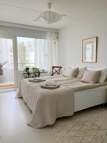 a white bedroom with a large bed and a window at Cozy apartment with free parking in Espoo