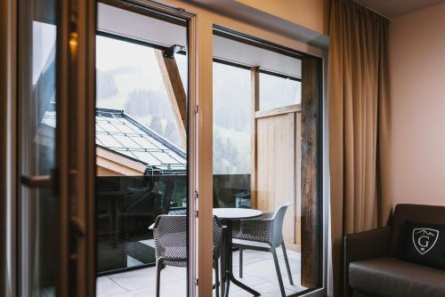 a room with a balcony with a table and chairs at GLEMM by AvenidA Superior Hotel & Residences in Saalbach Hinterglemm