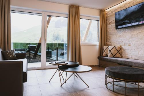 a living room with a fireplace and a large window at GLEMM by AvenidA Superior Hotel & Residences in Saalbach Hinterglemm